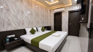 Habitación de hotel con pared de mármol, cama con ropa blanca y detalles verdes, mesita de noche con una botella y un ventilador de techo.