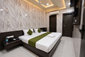 A hotel room with a marble wall, a bed with white bedding and green accents, a bedside table with a bottle, and a ceiling fan. - Hotel Hari Palace (Rajkot)