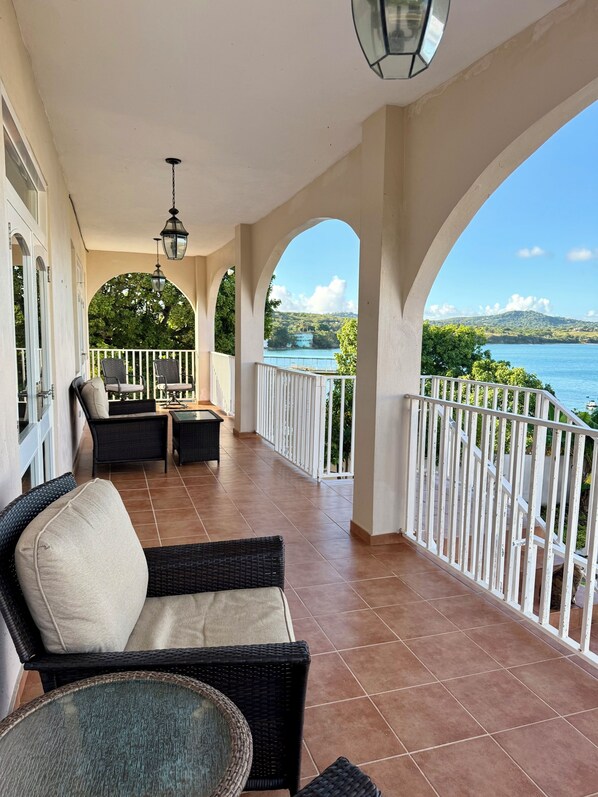 A covered outdoor seating area with wicker furniture and a view of a body of water.