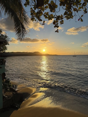 A beach scene with a sunset, calm sea, and a sailboat. - Frente Del Mar  Oceanfront Pool Villa  Walk to Ferry, Dining & Lighthouse (Vieques)