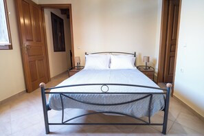 A bed with a metal frame, two bedside tables, and a wooden door in the background. - Seaside House | Mythos House • Symi • Sleeps 6 (Pedi)