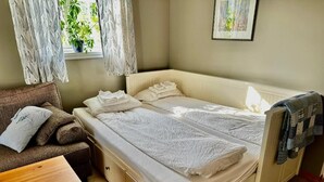 Ein kleines, aufgeräumtes Schlafzimmer mit einem Einzelbett, einem Schlafsofa und einem kleinen Tisch.