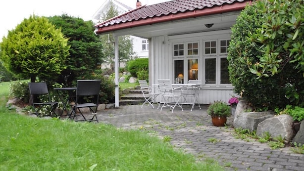 Ein überdachter Außenbereich mit Stühlen und Tischen, einem Topfpflanzen und einem Haus mit rotem Dach.