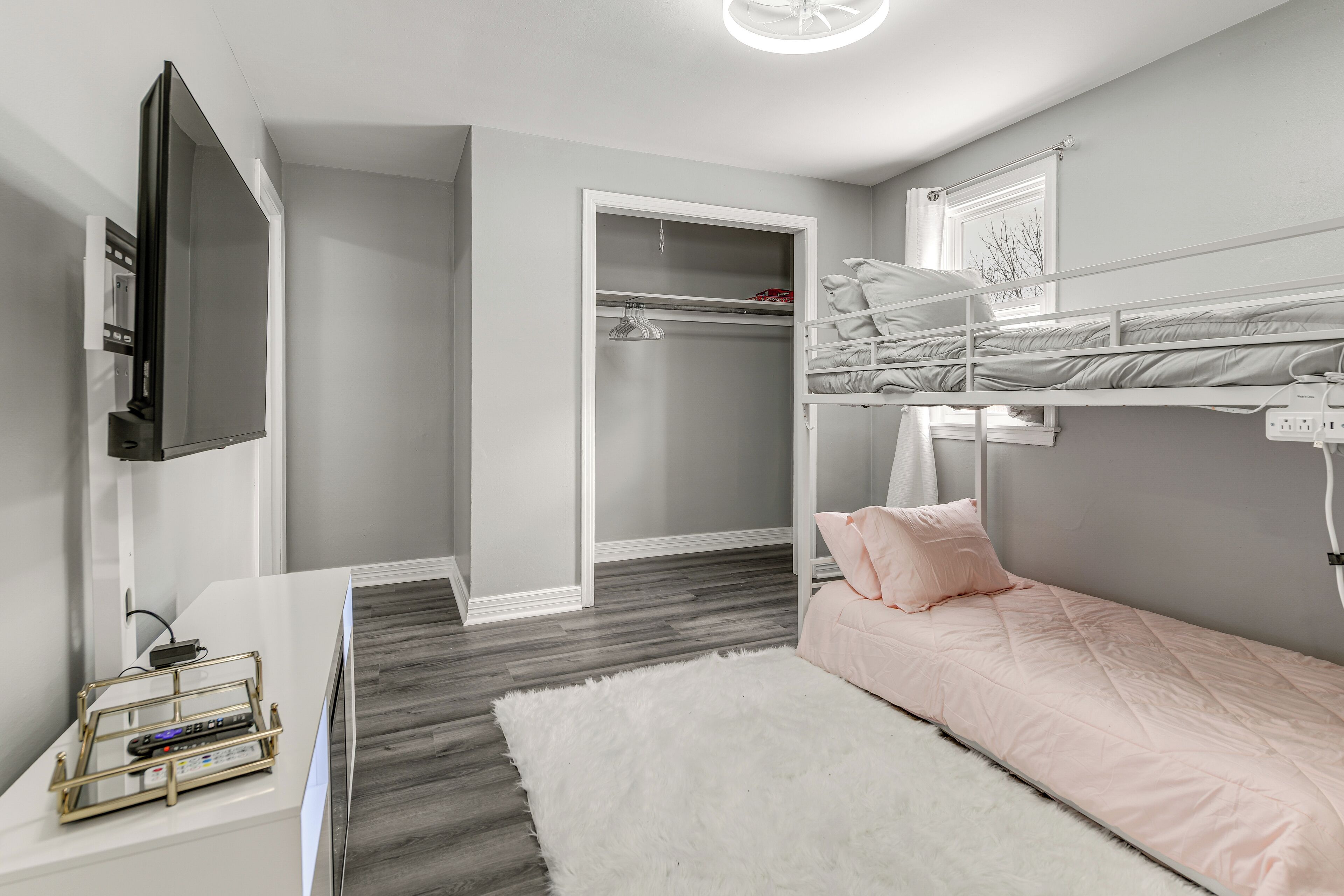 Ein modernes Schlafzimmer mit Etagenbett, einem weißen Schreibtisch mit Ladestation, einem flauschigen weißen Teppich und einem begehbaren Kleiderschrank.