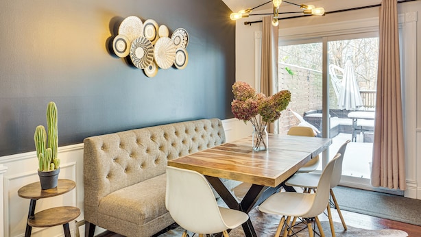 A dining area with a wooden table, white chairs, a tufted sofa, and a wall-mounted light fixture. - Faith-based Retreat: Peace, Restoration, Healing (Berea)