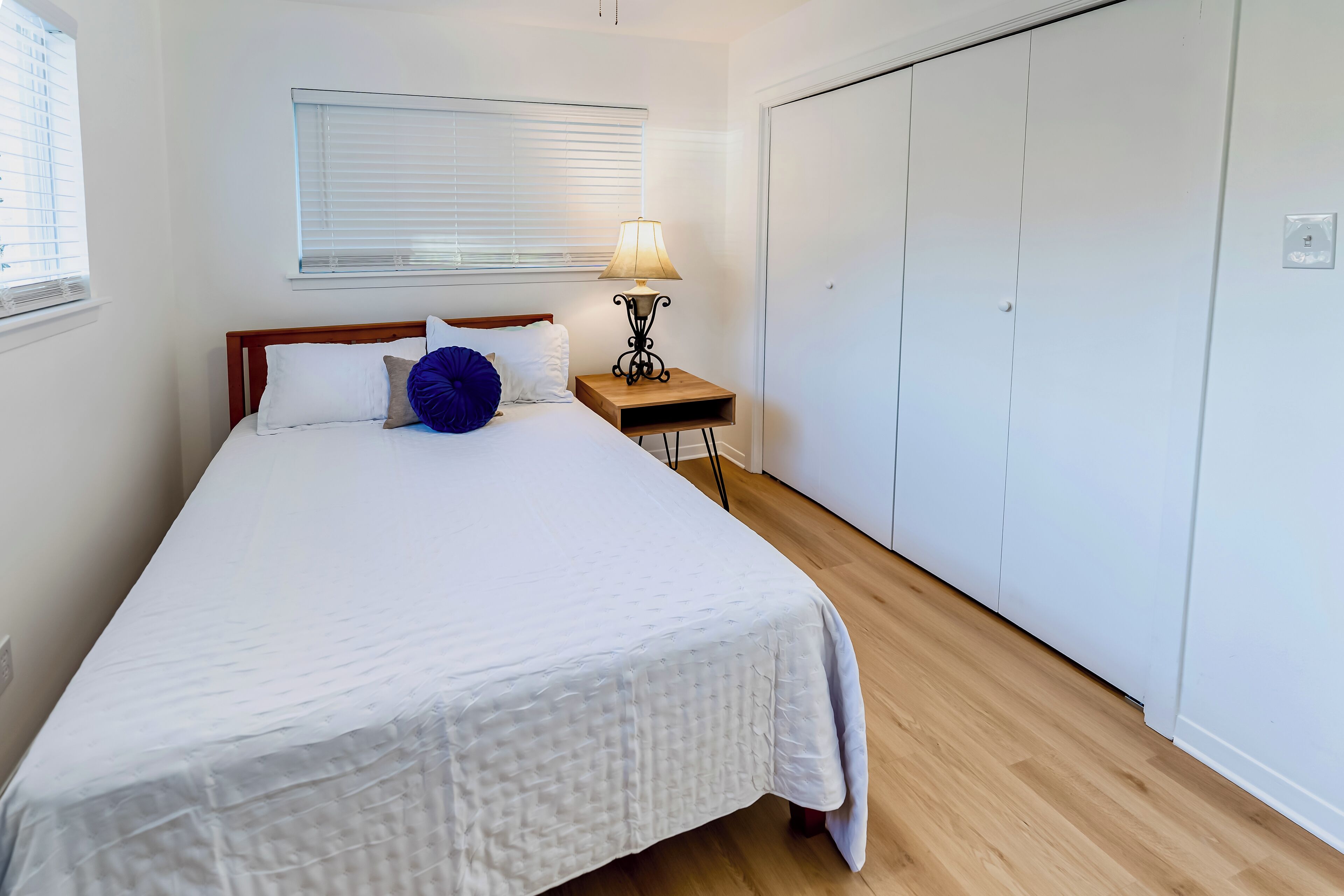 Un dormitorio con cama, mesita de noche con lámpara, armario y ventana con persianas.