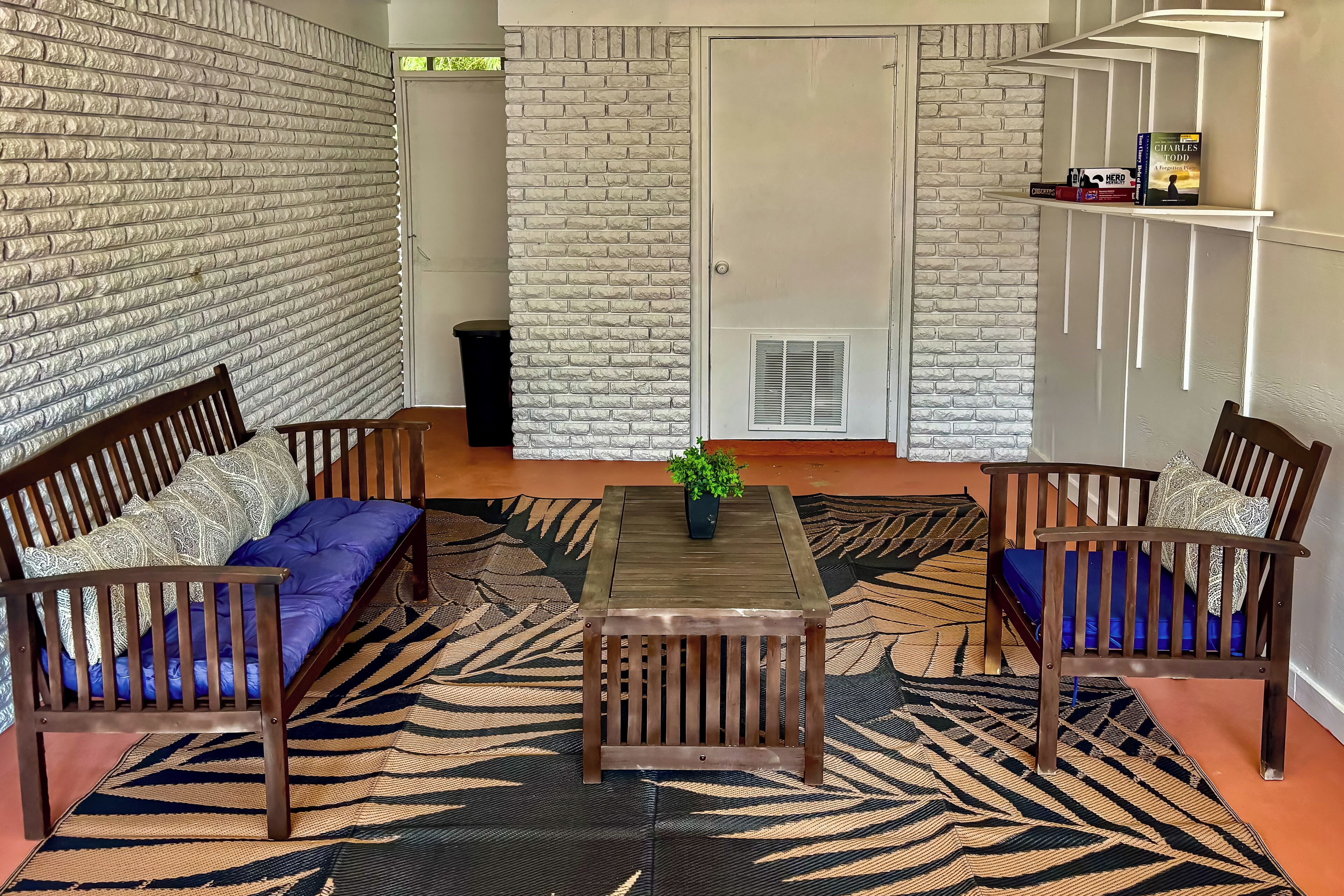 Una habitación con pared de ladrillo, un banco de madera, una mesa y un tapete estampado.