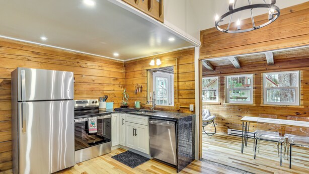 A modern kitchen with wooden paneling, stainless steel appliances, and a dining area with a table and chairs. - Pool, Beach & Lake Access: Poconos Cabin Escape! (Tobyhanna)