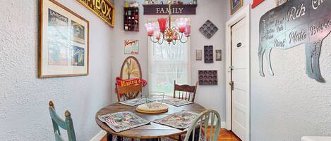 A dining area with a round table, chairs, a chandelier, and wall decorations including a sign that says "FAMILY".