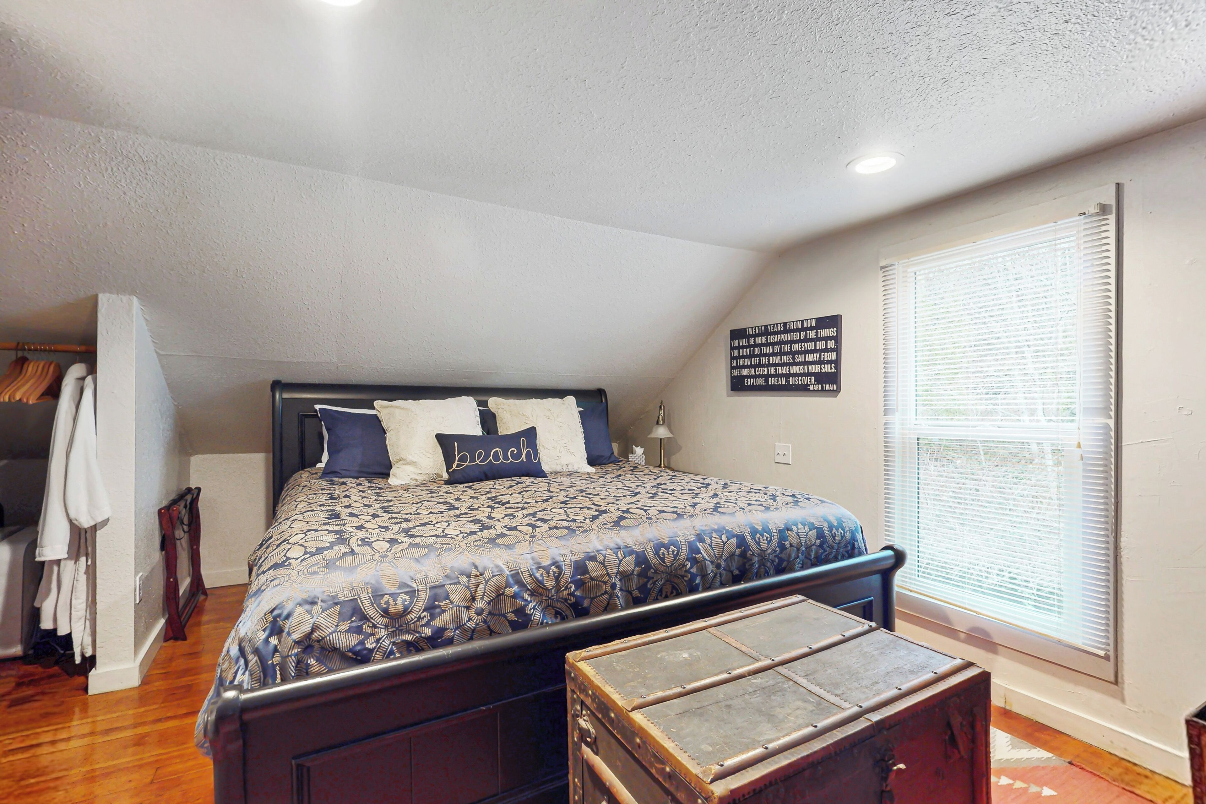 A bedroom with a bed, a wooden chest, a coat rack, and a window with blinds.