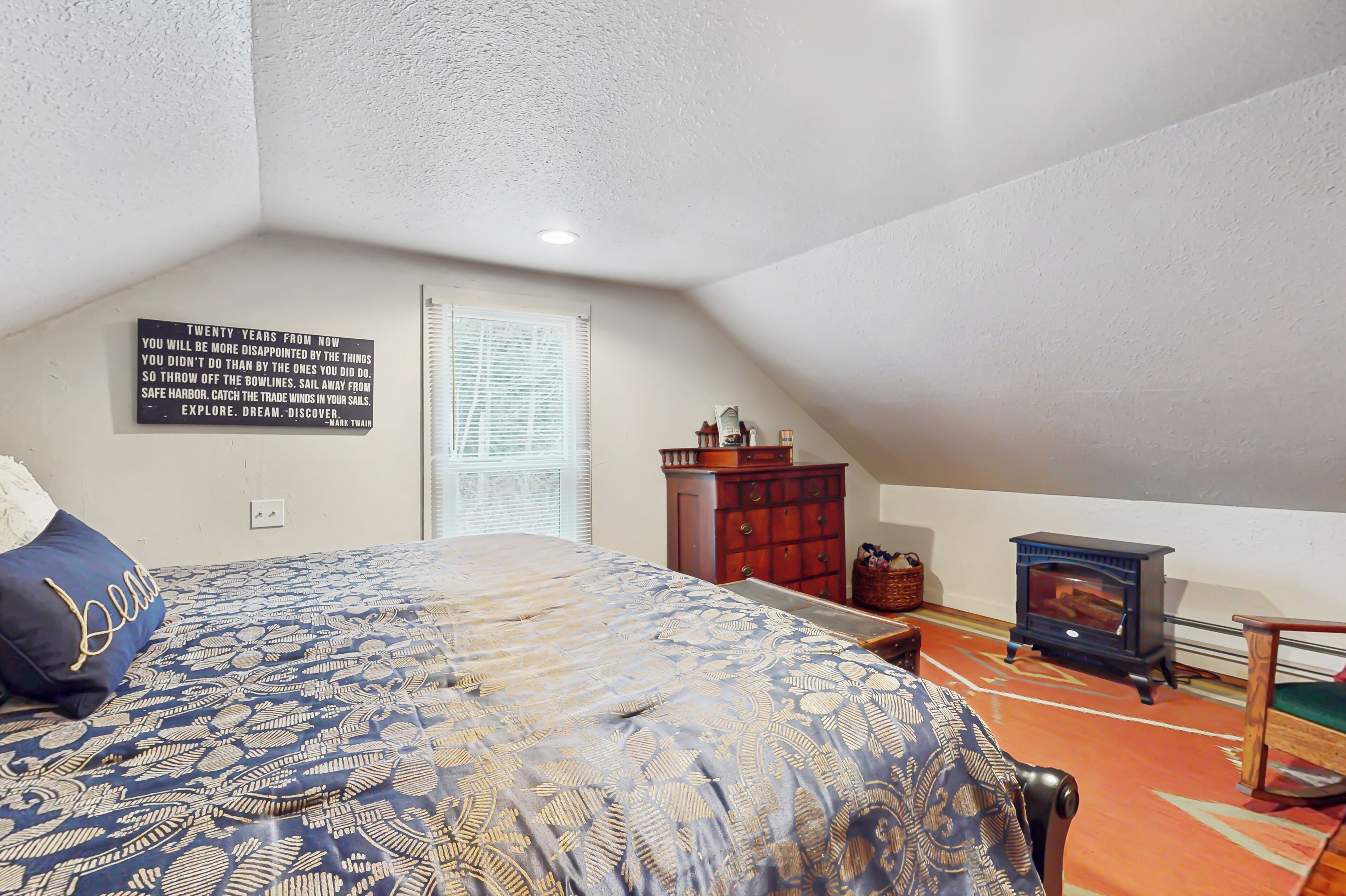 Un dormitorio con cama, cómoda, un pequeño calentador y una cita motivacional en la pared.