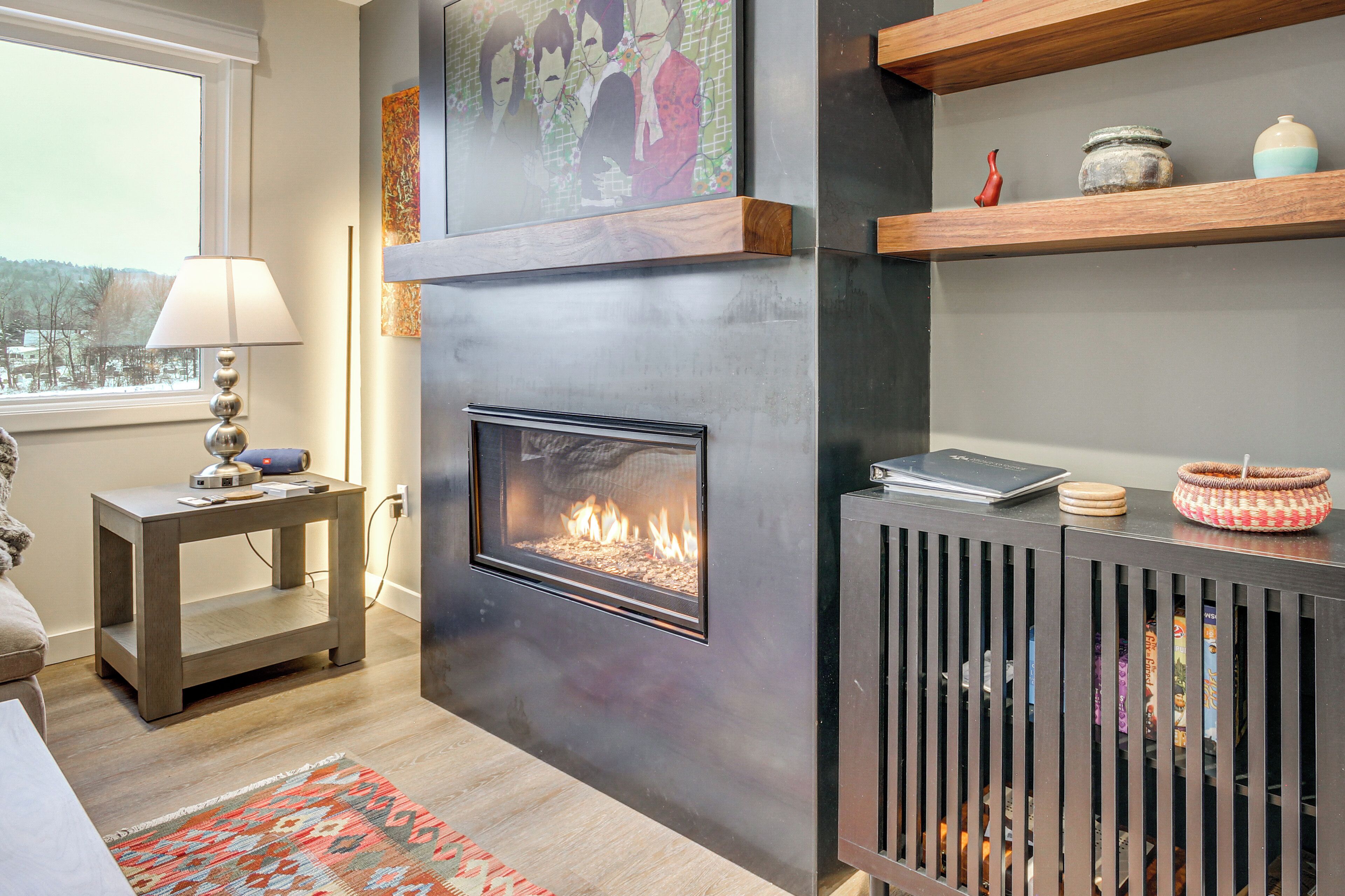A modern living room with a fireplace, wooden shelves, and a view of the outdoors.