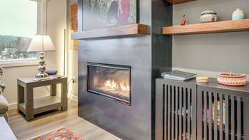A modern living room with a fireplace, wooden shelves, and a view of the outdoors.