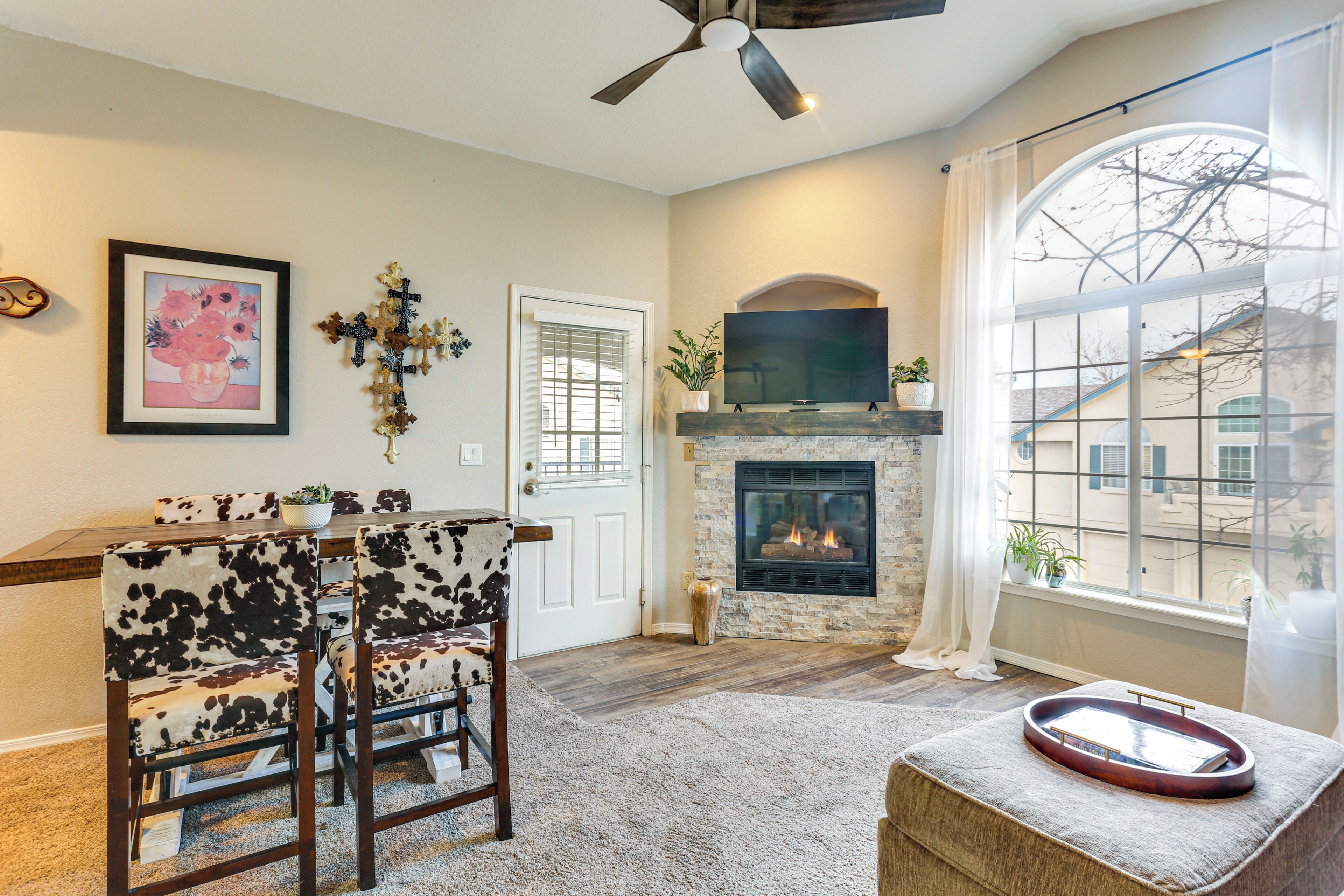 A living room with a fireplace, a dining area with a table and chairs, and a large window with a view of buildings.
