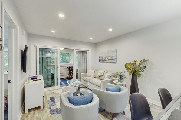 A modern living room with a sofa, armchairs, a glass coffee table, and a dining area with chairs and a table. - Hilton Head Haven: Beach House Lookout w/ Pool (Hilton Head Island)