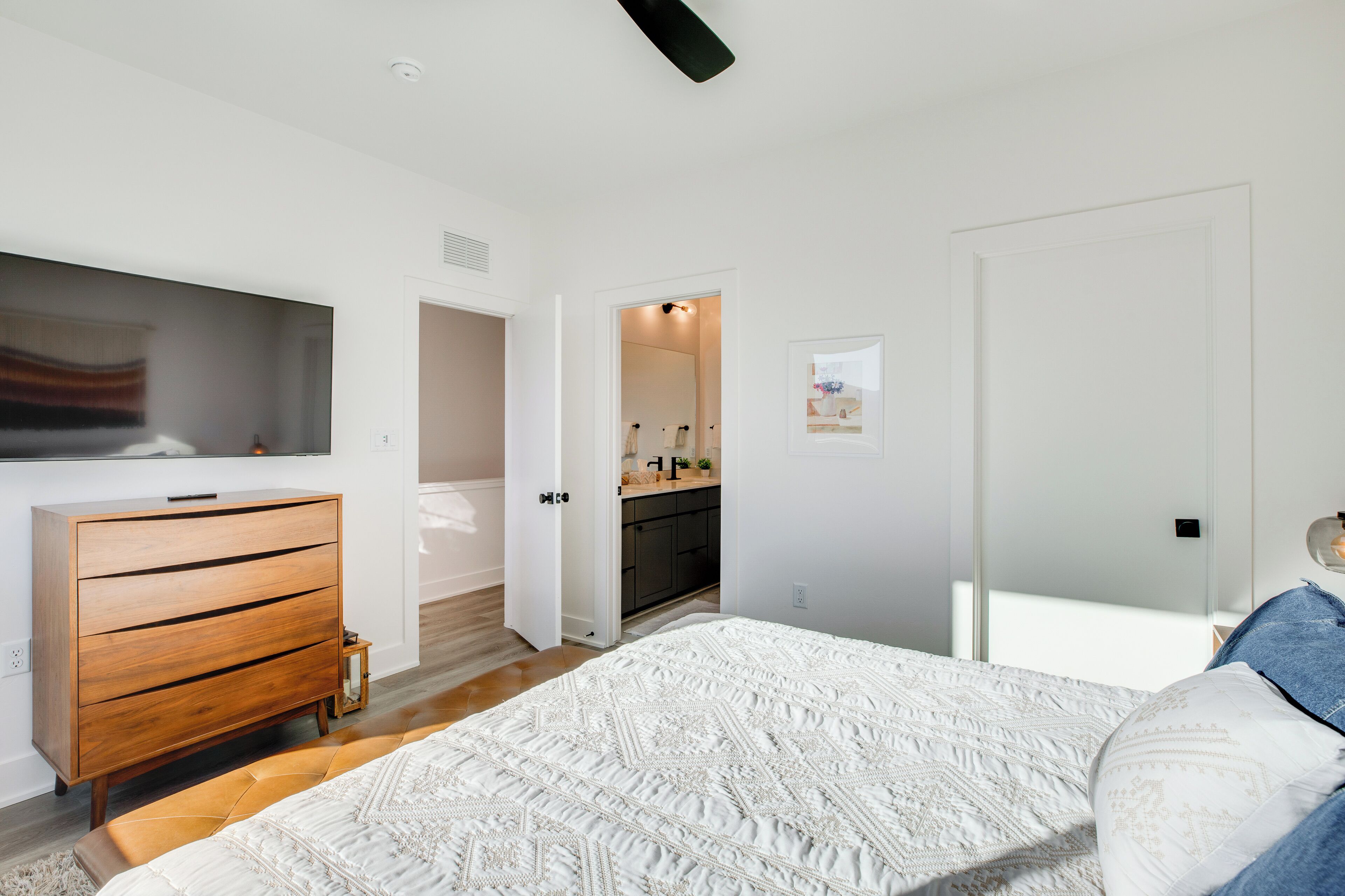 Una camera da letto con un letto grande, una cassettiera in legno, un bagno con specchio e una porta che conduce in un'altra stanza.
