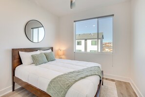 A bedroom with a large bed, a round mirror, a bedside lamp, and a window with a view of buildings.