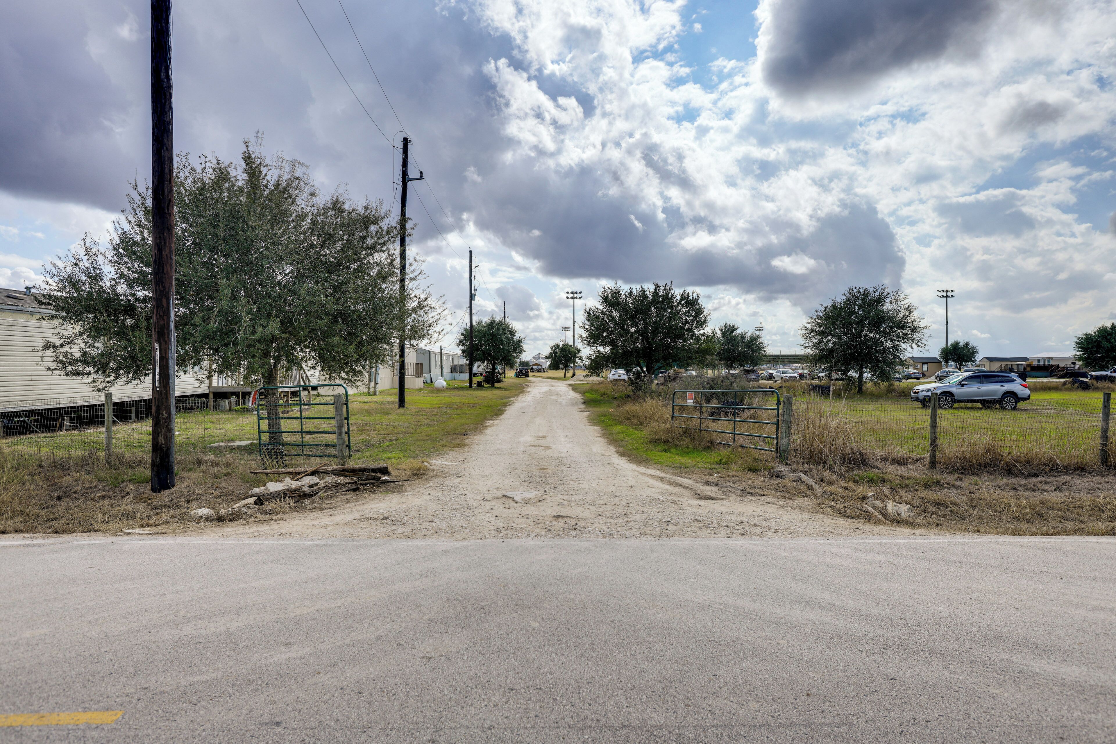 A rural road leading to a gated area with houses in the background.