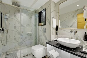 A modern bathroom with a glass-enclosed shower, a white toilet, a large mirror, and a black marble countertop. - Nanak Niwas Beacon New Delhi Paharganj (New Delhi)