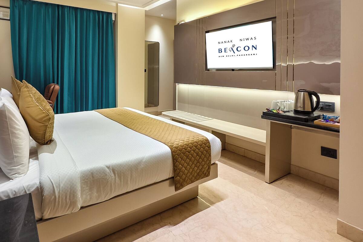 Quarto de hotel com cama, escrivaninha, televisão e cafeteira.