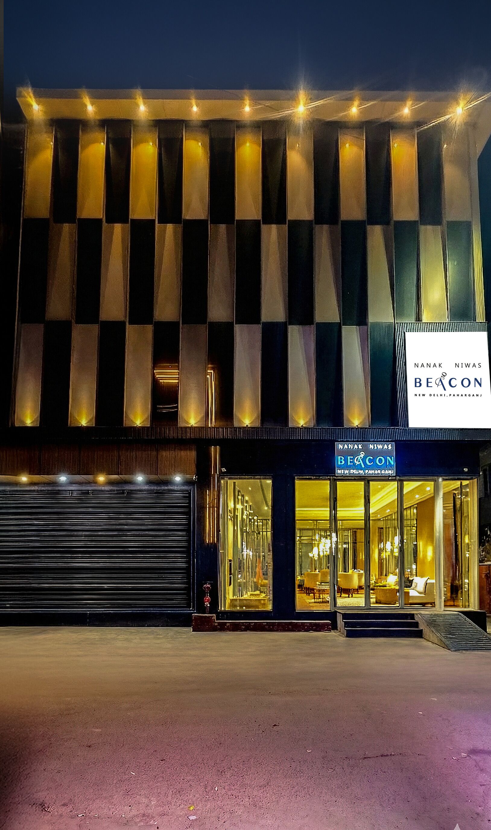 A hotel with a checkered facade, large glass windows, and a sign reading "Nanak Niwas Beacon New Delhi, Pharganj."