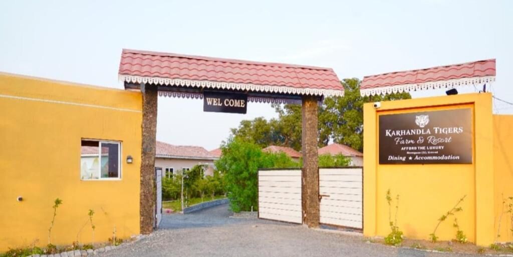 A yellow building with a 'Welcome' sign and a sign for 'Karhandla Tigers Farm & Resort' offering dining and accommodation.
