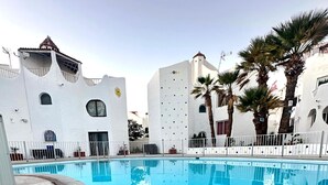 Ein Schwimmbecken mit Fliesen umgeben, umrahmt von weißen Gebäuden mit markanter Architektur.