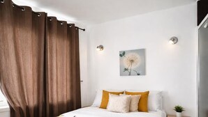 Ein modernes Schlafzimmer mit einem großen Bett, einem Nachttisch, einer Fensterbank mit Vorhängen und einer Wandleuchte.