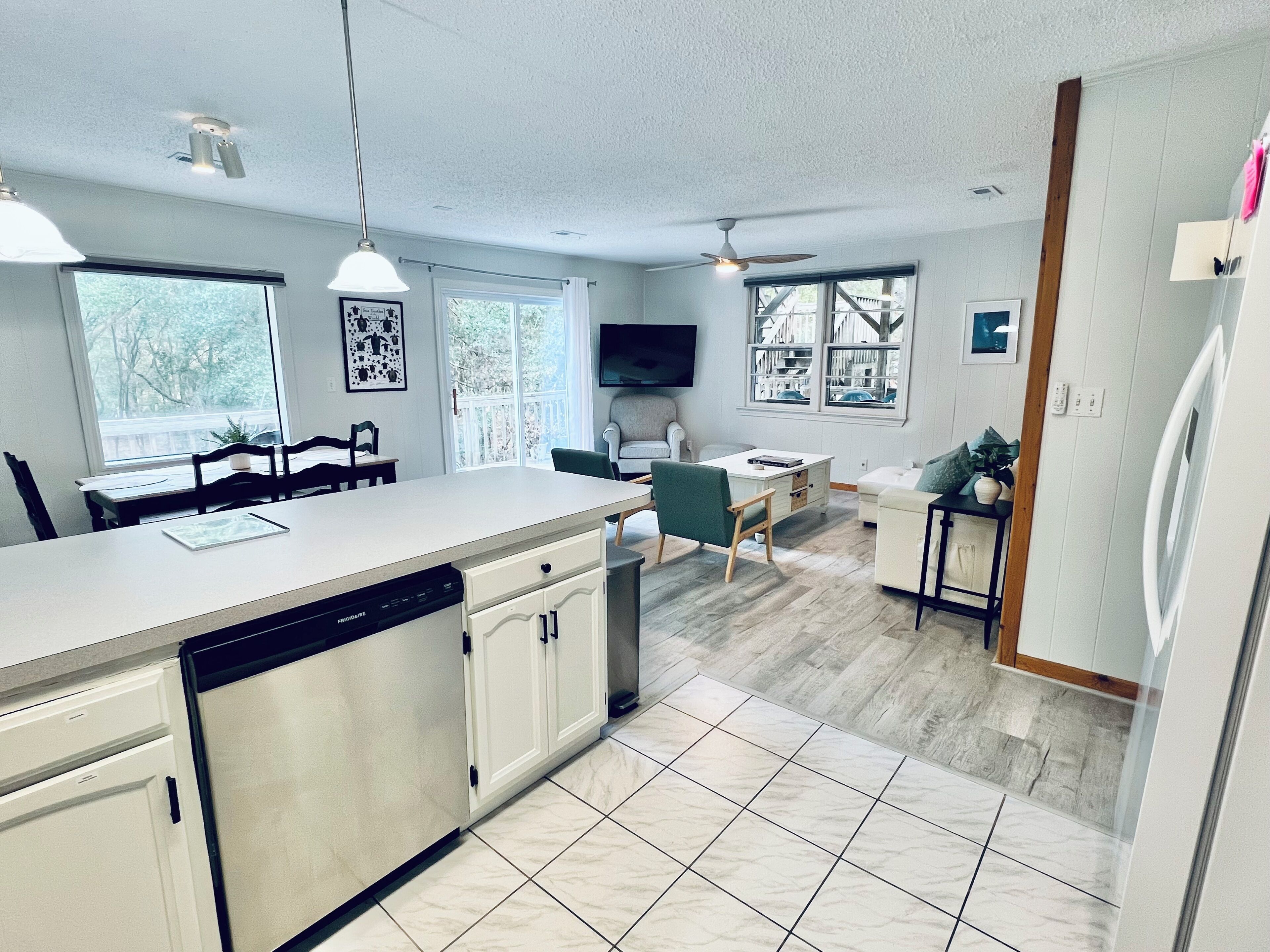 A modern kitchen with a dishwasher, a dining area with chairs, a TV, and a ceiling fan.