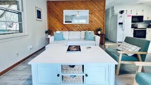 A modern living room with a white sofa, a wooden accent wall, a white coffee table, and a teal armchair. - Pets, Pool & Spa - Tranquil Treetop Family Home (Kitty Hawk)