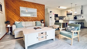 A modern living room with a wooden accent wall, a white sofa, a coffee table, and a green armchair. - Pets, Pool & Spa - Tranquil Treetop Family Home (Kitty Hawk)