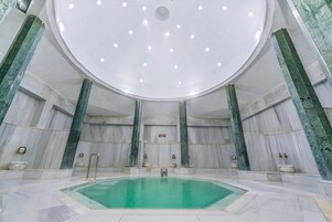 Una amplia piscina interior con techo circular y paredes de mármol.