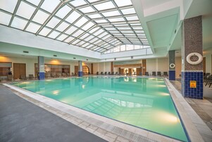 Una piscina interior con techo de tragaluces, sillones de descanso y puesto de socorrista.
