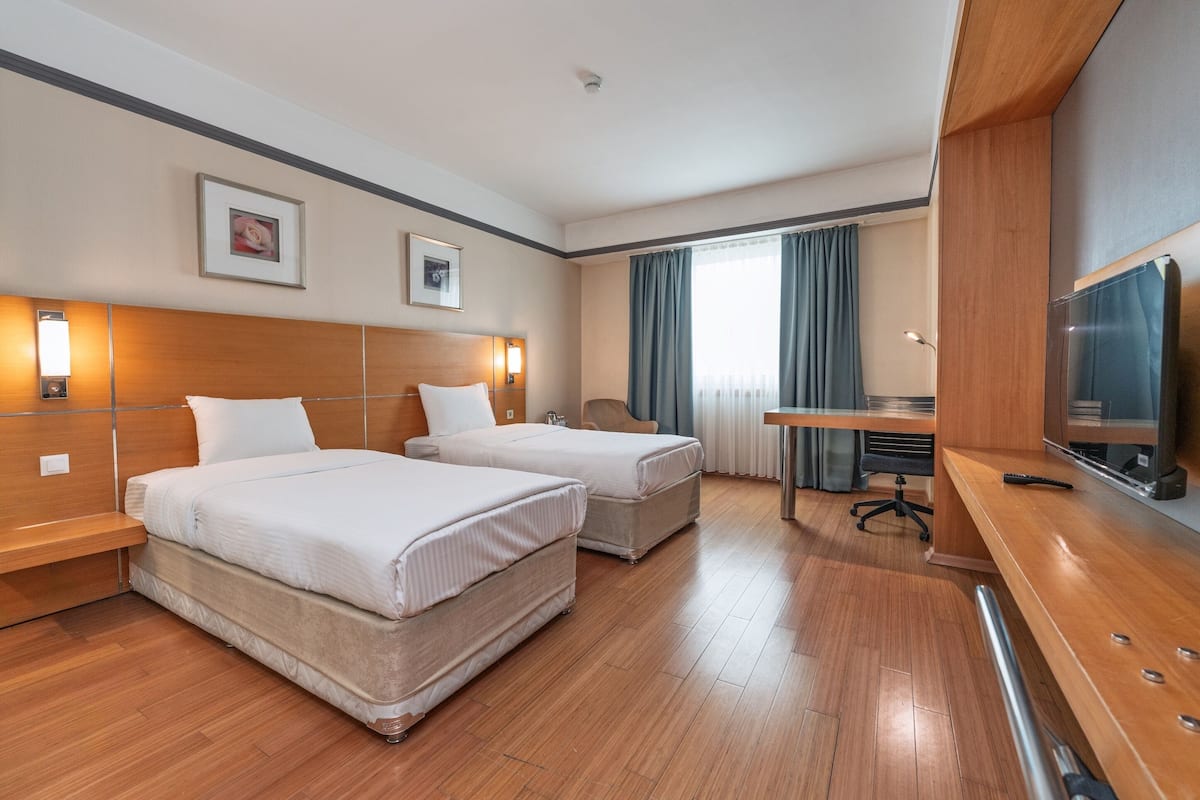 Habitación de hotel con dos camas, un escritorio, una silla, un televisor y una ventana con cortinas.