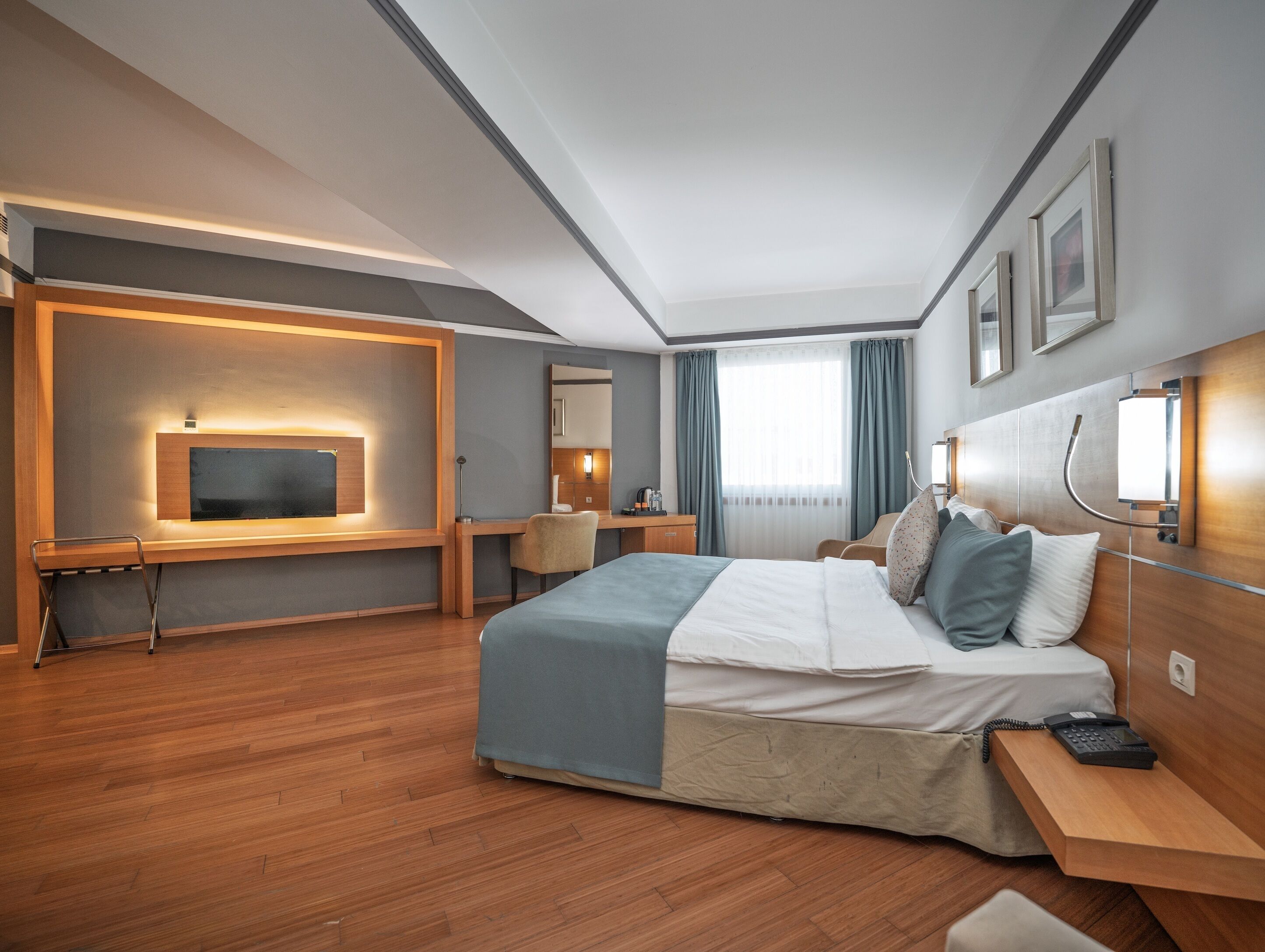 Una habitación de hotel moderna con una cama grande, un escritorio con silla, un televisor montado en la pared y un área de ducha.