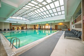 An indoor swimming pool with a glass ceiling, lounge chairs, and a reception area.