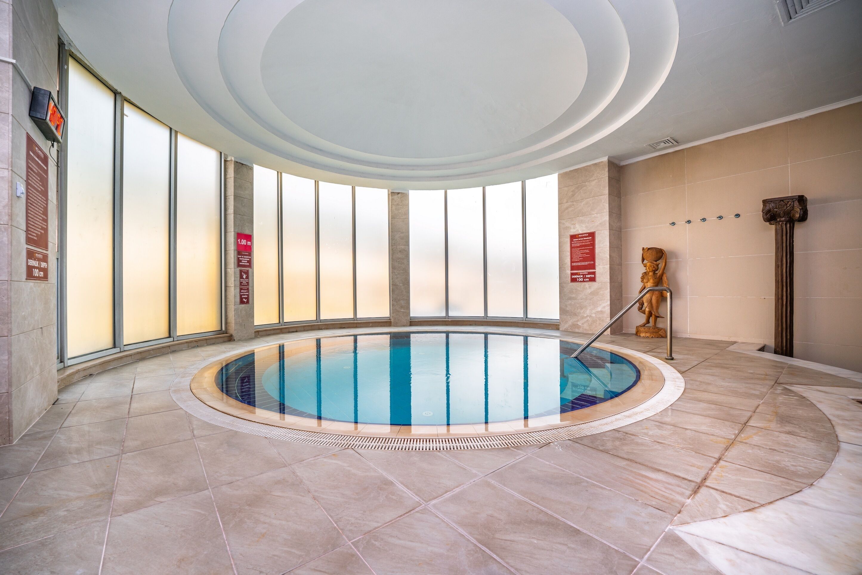 A large indoor swimming pool with a tiled floor and a central column.