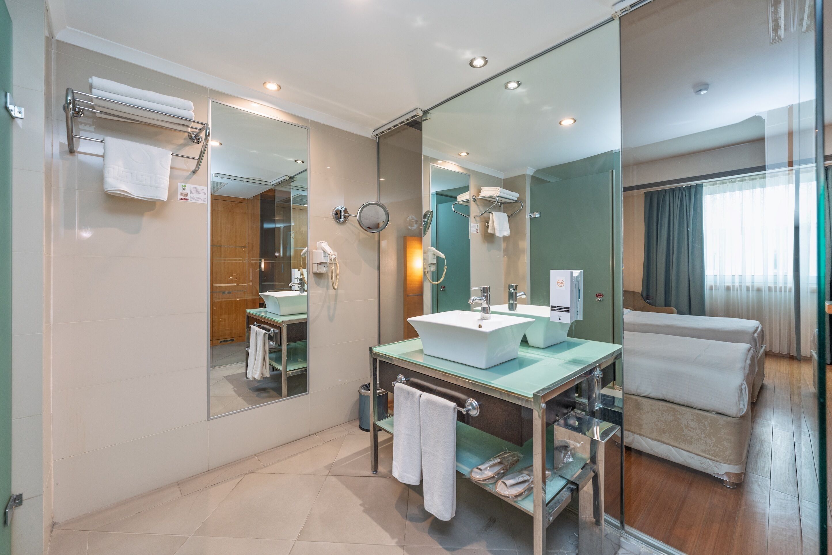 Een moderne badkamer met een douche met glazen wand, een wastafelmeubel en een bed met een glazen scheiding.