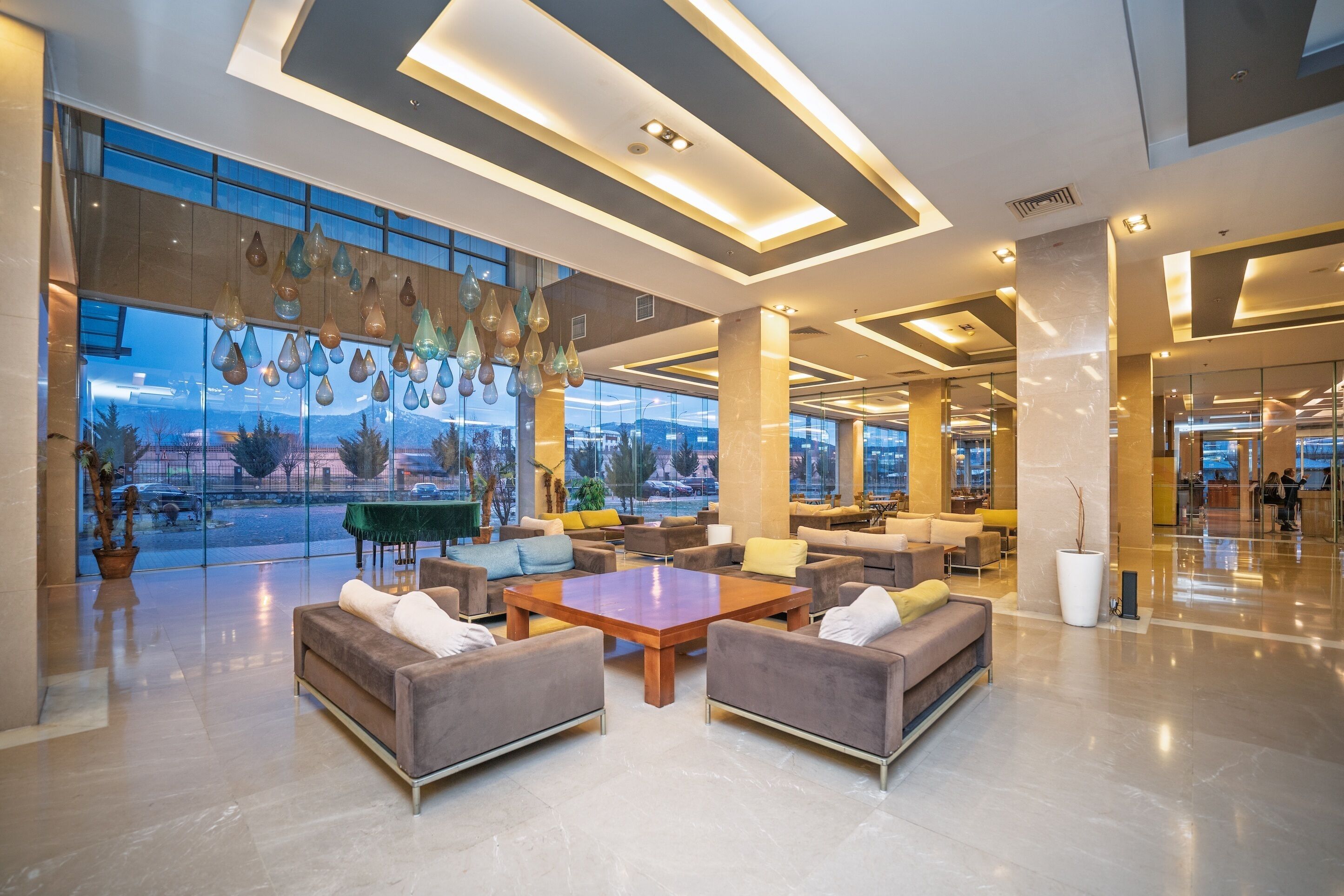 Un vestíbulo amplio con muebles modernos, ventanas grandes y lámparas colgantes.