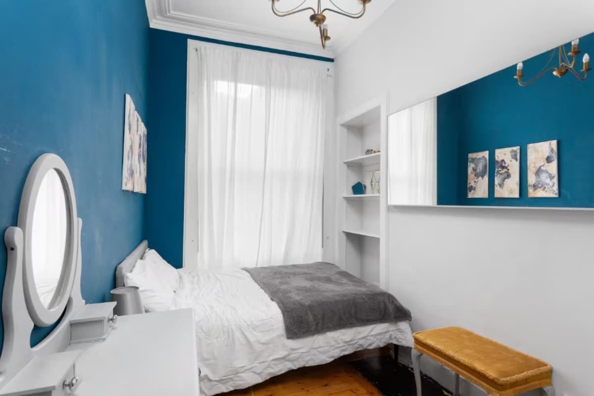 Une chambre à coucher comprenant un lit, une coiffeuse avec un miroir, un banc et des œuvres d’art accrochées au mur.