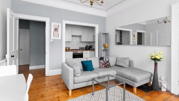 A modern living room with a grey sofa, a glass coffee table, and a patterned rug. - First Floor-2 Bedroom Apartment (Edinburgh)