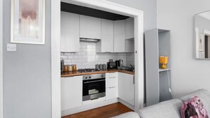 A compact kitchen with white cabinets, a stove, and a microwave. - First Floor-2 Bedroom Apartment (Edinburgh)