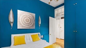 A bedroom with a bed, two pillows, a bedside table, a wall hanging, and a wardrobe. - First Floor-2 Bedroom Apartment (Edinburgh)