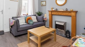 A living room with a grey sofa, a wooden coffee table, a fireplace, and a mirror on the wall. - Large 4 Bed House - 4 Double Beds (Barrow-in-Furness)