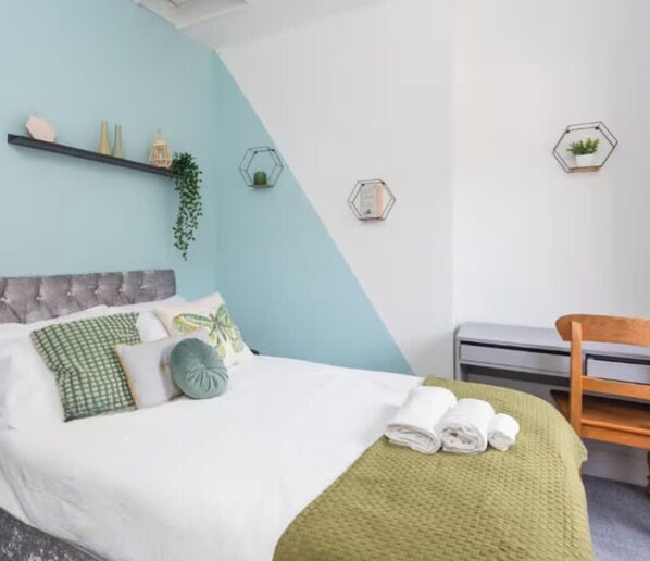 A modern bedroom with a bed, a green blanket, and a wooden chair. - Large 4 Bed House - 4 Double Beds (Barrow-in-Furness)