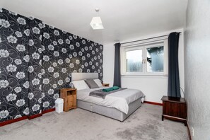 A bedroom with a bed, a nightstand, a dresser, a window with curtains, and a wall with a floral pattern. - 4 Bedroom House - Free Parking (Aberdeen)