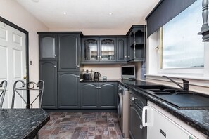 A modern kitchen with dark cabinetry, a built-in oven, and a window overlooking the city. - 4 Bedroom House - Free Parking (Aberdeen)
