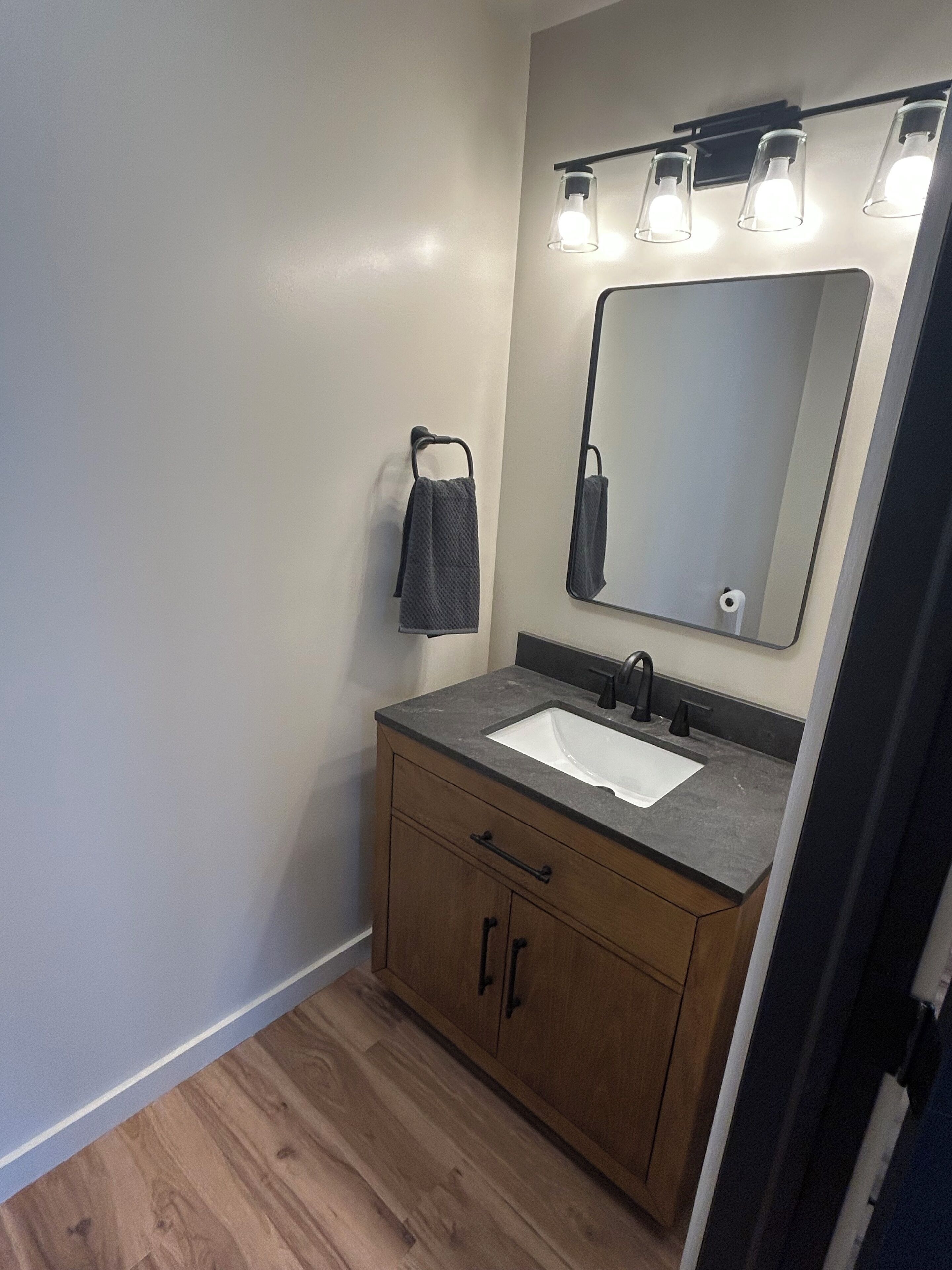 Un baño con tocador de madera, un lavabo blanco, un espejo y un perchero para toallas.
