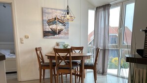 A dining area with a wooden table and chairs, a pendant light, and a painting on the wall. - Cozy apartment with sea view in Lemkenhafen (Fehmarn)