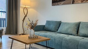 Un saló modern amb una taula baixa de fusta, un sofà verd, una làmpada de peu i una finestra gran amb cortines.